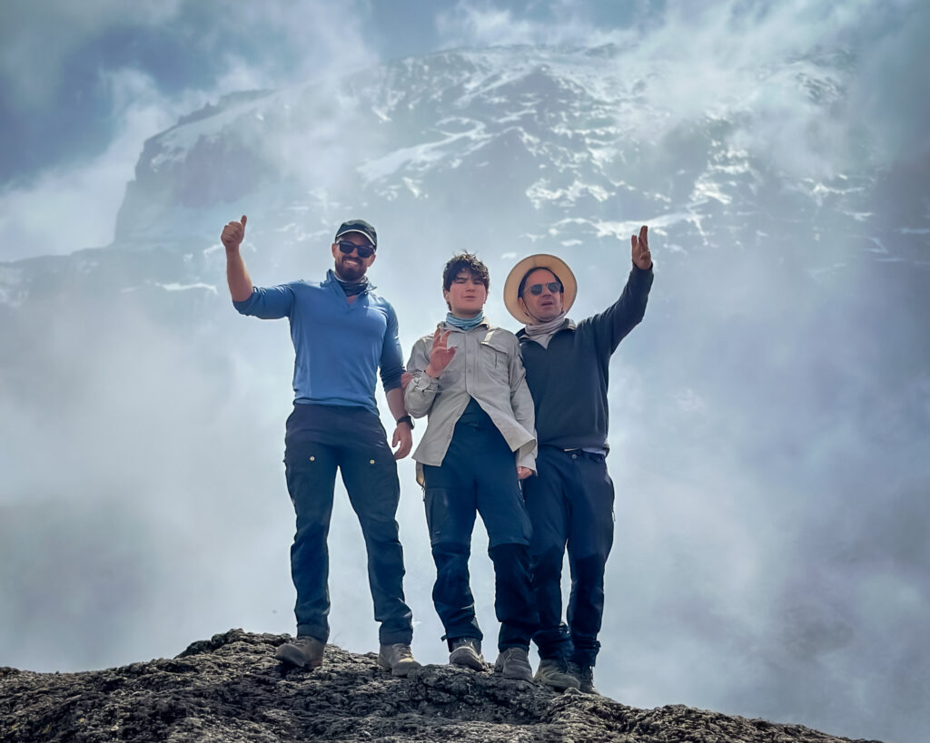 Sam Abboud, 13-year-old Christopher Abboud, and Tom Hamill on top of the Barranco Wall with the massive Kibo Crater of Mount Kilimanjaro emerging from the fog.
