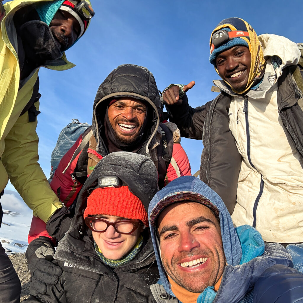 Rami Rasamny with 13-year-old Christopher Abboud and LHO guides Asseno, Saidi, and William standing together at Stella Point on Mount Kilimanjaro.