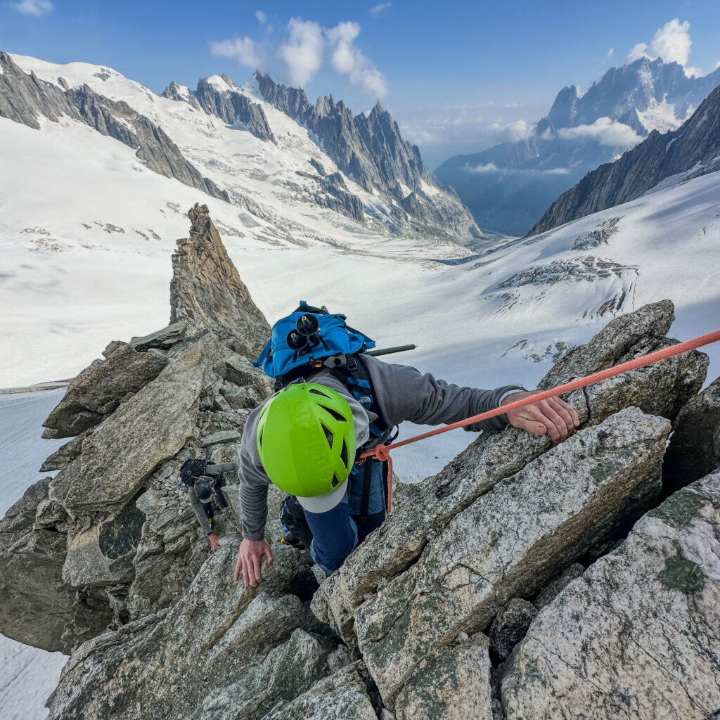 Life Happens Outdoors community member climbing the Petit Flambeau on a rocky dry ridge in big mountaineering boots during the Mont Blanc Summit Course, featured in the article Can I Climb Mont Blanc as a Beginner.