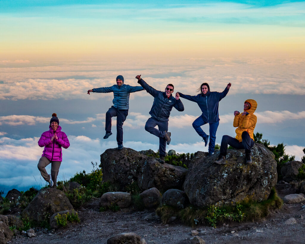 Life Happens Outdoors community members enjoying a golden sunset on the Marangu Route with Mount Kilimanjaro’s peaks glowing in the evening light.