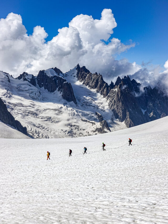 Life Happens Outdoors corporate team roped together walking across the Vallée Blanche glacier in Chamonix, surrounded by towering Alpine peaks and clear blue skies.
