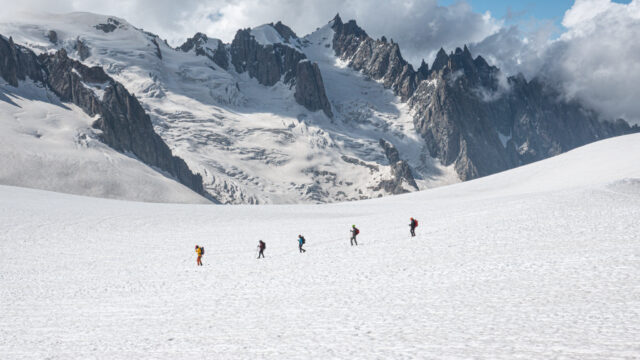 Life Happens Outdoors corporate team roped together walking across the Vallée Blanche glacier in Chamonix, surrounded by towering Alpine peaks and clear blue skies.