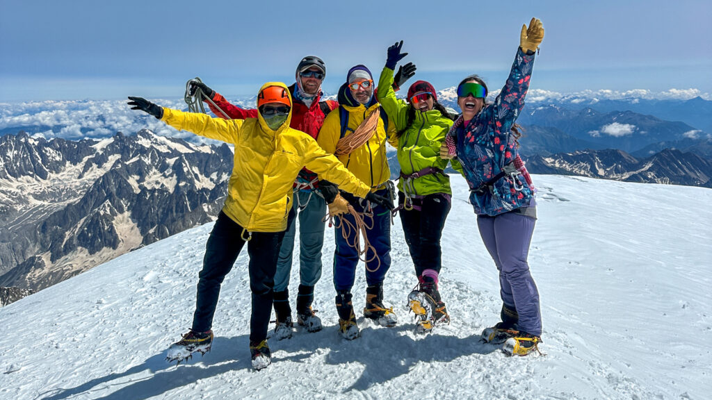 Life Happens Outdoors team stands on the summit of Mont Blanc under clear skies, celebrating a successful ascent with panoramic views of the Alps.