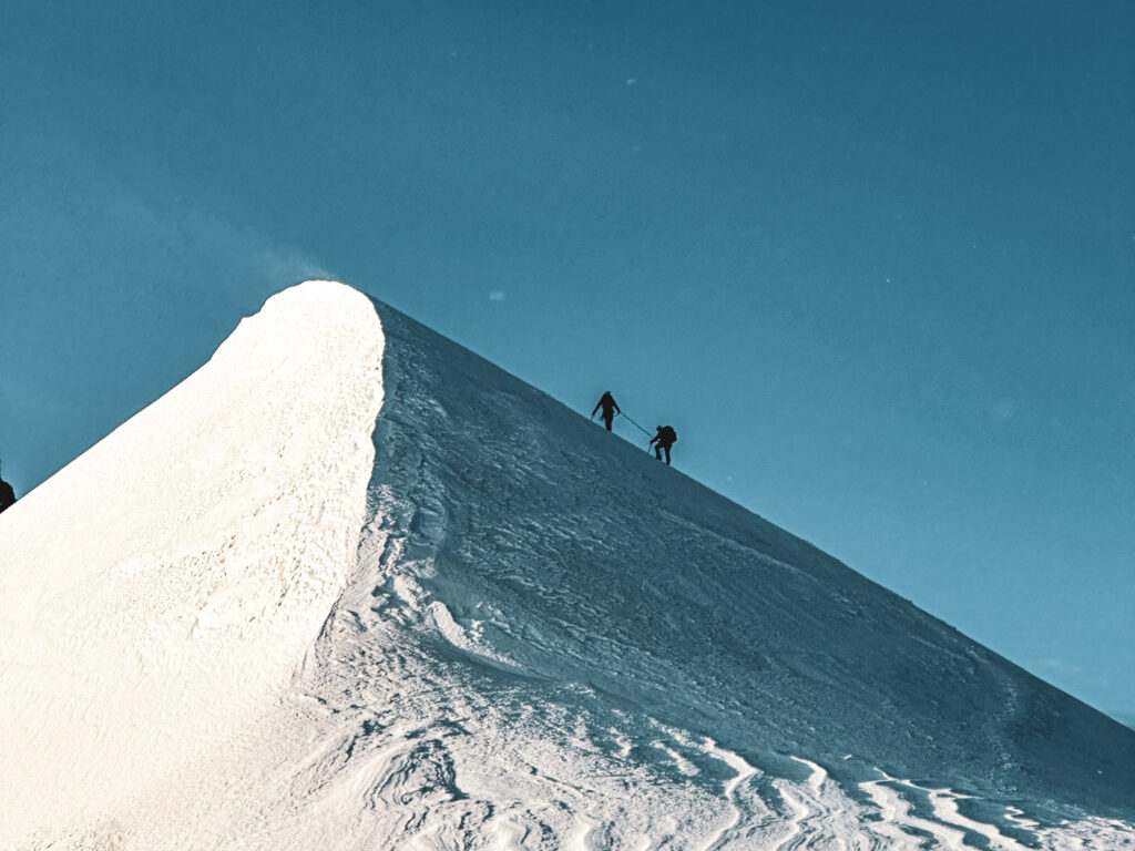 A Life Happens Outdoors rope team standing on top of the first mogul on Mont Blanc, pausing to rest and take in the early morning alpine views.