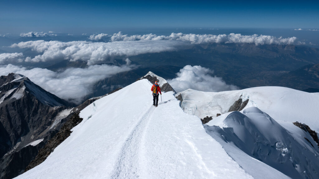 Team of first time climbers descending the Mont Blanc summit ridge in clear weather with wide views over the Haute Savoie alpine region.