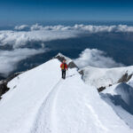 Team of first time climbers descending the Mont Blanc summit ridge in clear weather with wide views over the Haute Savoie alpine region.