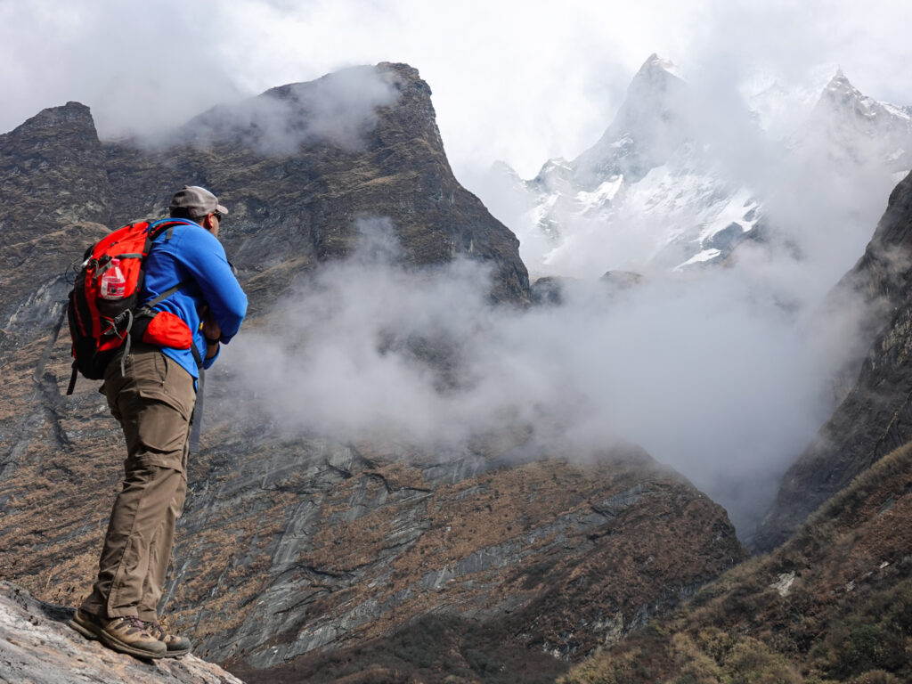 Life Happens Outdoors trekker observing Machapuchare’s summit near Himalaya Tea House on the Annapurna Base Camp trek, surrounded by steep mountain walls and rising valley clouds.