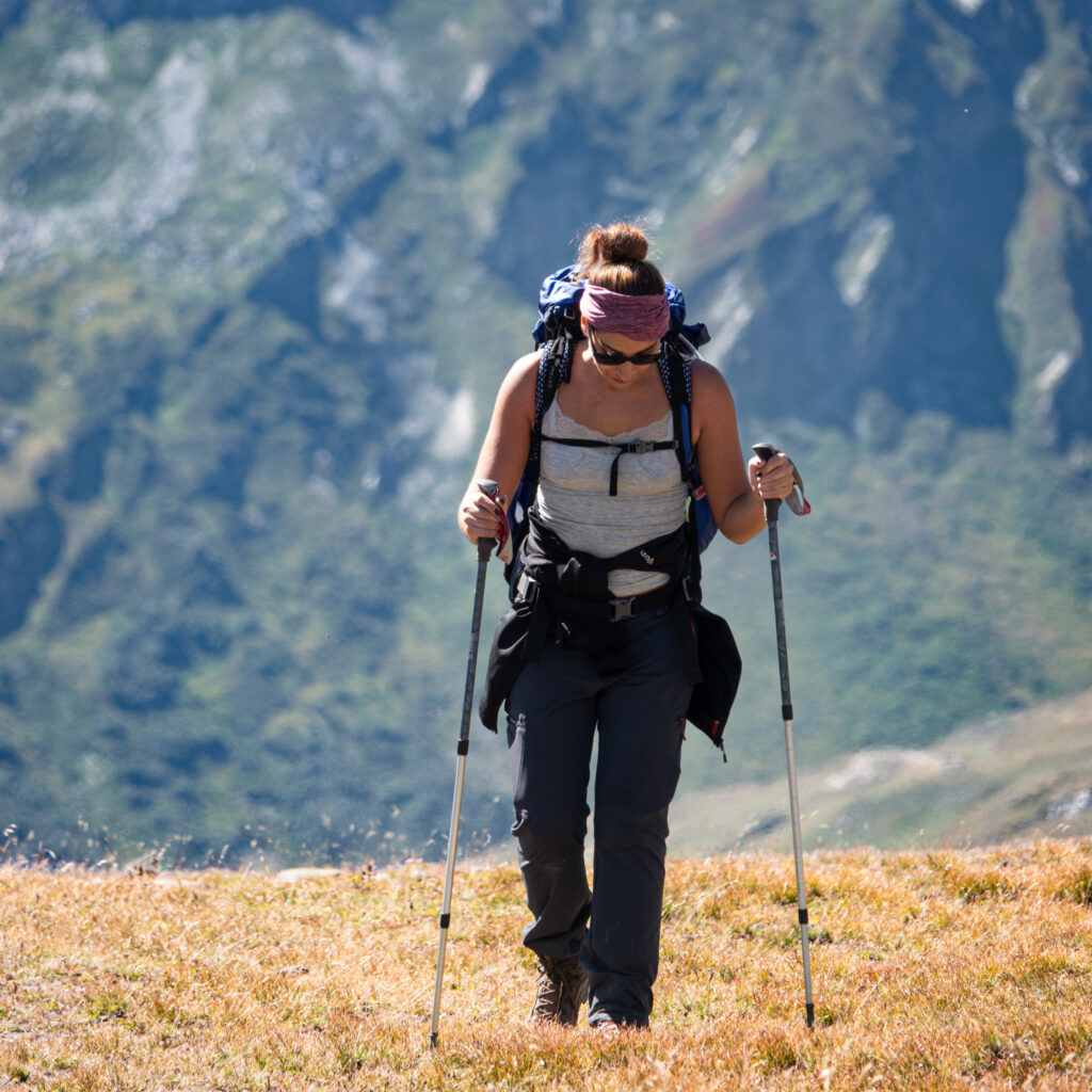 Life Happens Outdoors community member hiking a grassy alpine ridge on the Tour du Mont Blanc during a sunny summer ascent.