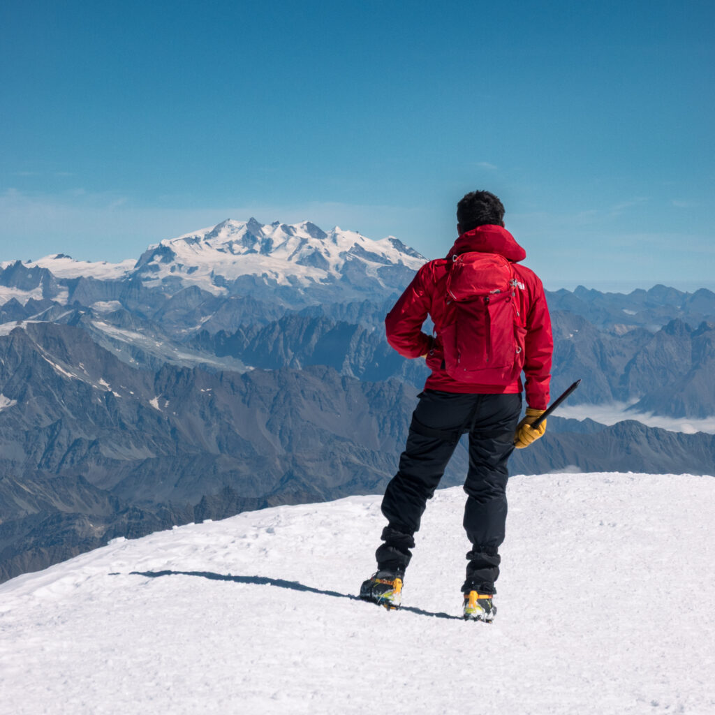 First time climber from the Life Happens Outdoors community standing on the Mont Blanc summit with panoramic views toward Monte Rosa on a perfect clear day.