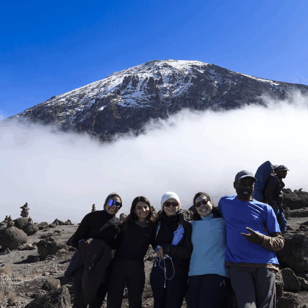 Life Happens Outdoors all female team full of energy before summit day on Kilimanjaro with Kibo crater visible and blue skies
