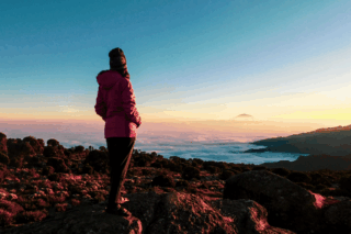Life Happens Outdoors community member enjoying sunset views of Mount Meru and a sea of clouds while on Kilimanjaro.