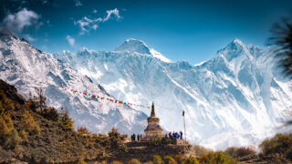 Buddhist stupa and prayer flags beneath snow covered Himalayan peaks in Nepal