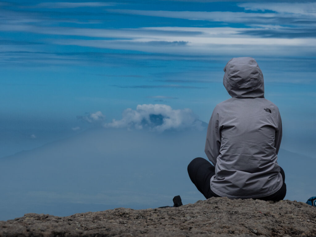 Life Happens Outdoors community member resting on Machame Route with Mount Meru on the horizon under a blue sky