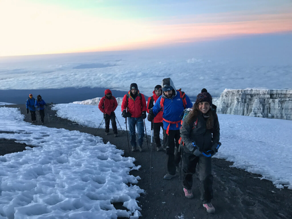Group of trekkers walking near Kilimanjaro glaciers at dawn on the summit route.