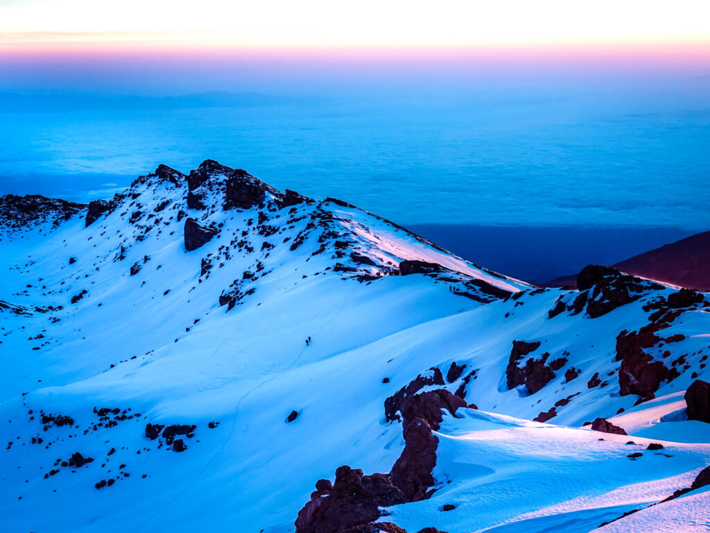 Snow covered ridge on Kilimanjaro during blue hour above a sea of cloud.